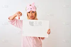 中年妇女戴着睡眠面罩，在孤立的白色背景上举着旗帜，愤怒的脸，消极的迹象显示不喜欢用拇指，拒绝的概念