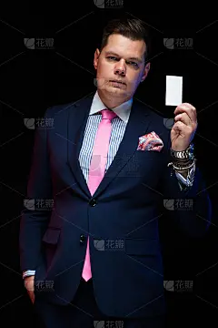 肖像自信英俊的商人拿着名片在他的手在黑色的背景与手在口袋