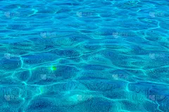 海洋背景。透明的蓝绿色海水的背景白色的沙子下面，俯视图。太阳在表面刺眼。高质量的照片
