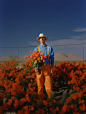 this highly realistic photographic portrait shows a man posing in orange pants and hat with orange flowers and blue shirt , in the style of matthew barney, stephen shore, desertwave, primary colors, full body, stanley pinker, no flowers in the ground, pun
