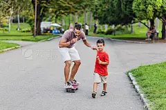 It’s important to set aside time for outdoor playPhoto of young hipster father and son having a ice cream while Skateboarding, holding hands in the street, family and parenthood. People having fun outdoors. Concept of friendly family. Father riding Skateb