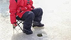 鳟鱼冰上钓鱼。一个男孩拿着钓竿在冰洞里等着。