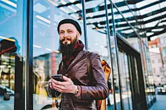 千禧一代的潮男脸上带着微笑，手里拿着智能手机，想着在莫斯科的周末，快乐的男游客在等待酒店的电话确认预