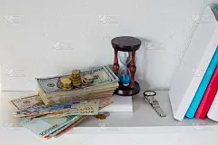 钱，沙漏和白色书架上的书。时间就是金钱的观念。