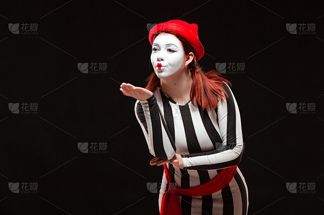 女哑剧艺术家表演的肖像，孤立在黑色背景上。一名身着条纹裙的女子摆出飞吻姿势