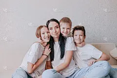 一个快乐的妈妈坐在家里的沙发上，怀抱着她的孩子们。理解支持对田园概念的信任