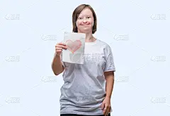 年轻的成年妇女与唐氏综合症持有红心卡在孤立的背景与快乐的脸站着，微笑着自信的微笑显示牙齿