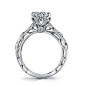 Elegant leaves and vines of milgrained 18K gold and diamonds climb towards a 6 prong crown holding a brilliant round center. Open and intricate filigree work float in the profile completing this vintage inspired stunner from the Lyria Bridal Collection. D
