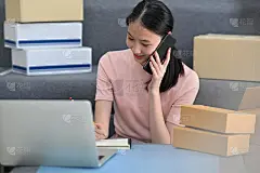年轻美丽的女孩坐在现代的客厅里，用手机聊天，在笔记本上写字。中小企业创业和网上市场的概念。