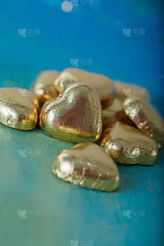 在一张古老的蓝绿桌子上放着用金箔纸包着的心形巧克力。用散景模糊背景。婚礼贺卡魅力卡