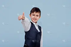 一个快乐的小孩穿着衬衫和背心，在蓝色的背景上指着手指和大拇指，看着相机