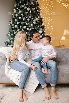 爸爸的画像，妈妈和儿子坐在家里靠近圣诞树的地板上，都面带微笑。牛仔布和白衬衫。圣诞节的家庭。幸福