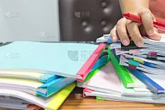 老师手查报告论文和学生作业，以核对成绩。档案里堆满了五颜六色回形针的未完成的文件。商业教育理念。
