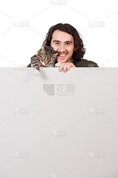一个兴高采烈的年轻人抱着他可爱的宠物猫，站在一个空白的广告和信息横幅后面。空白页，文本公告的复制空间