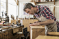 An antique furniture restorer in his workshop using a hand tool to smooth a wooden object.  by Mint Images on 500px