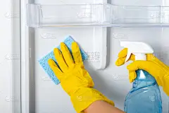  女人的手戴着黄色的橡胶防护手套和蓝色的海绵洗，清洗冰箱架子。清洁服务，家庭主妇，日常家务活。玻璃及