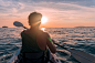 皮划艇。 有皮船桨的人在划船对太阳的日落海。