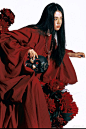 This may contain: a woman with long black hair in a red dress holding a black vase and flowers