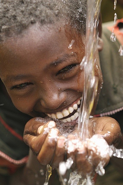 一个孩子在非洲的欢乐体验新鲜井水首次。