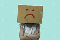 小女孩头上戴着一个纸板箱unglücklich，蓝色背景上孤立。
