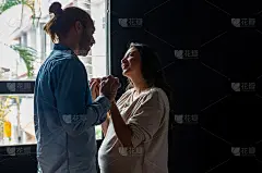 微笑的白种人丈夫牵手与他美丽的怀孕的妻子和看着她的脸与爱。夫妻在家里有浪漫的时刻。家庭纽带关系与孕产