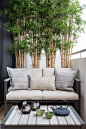 small balcony enclosed with medium high wall with low bench for two with white cushion and small coffee table, and some small bamboo plants on pots of Adding More Privacy to the Balcony