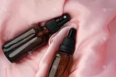 Etic瓶血清和滋补品。两个玻璃瓶子粉红色的丝绸顶视图。棕色玻璃容器