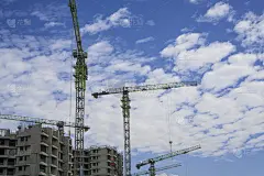 向上看高大的塔吊，移动机器和建筑在施工工作，脚手架在顶层，下白色蓬松的云清澈的蓝天