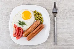 Fried egg and sausages with green peas, tomatoes in plate