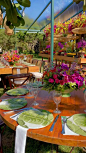 This may contain: an outdoor dining area with tables and chairs covered in flowers, plates and glasses on the table