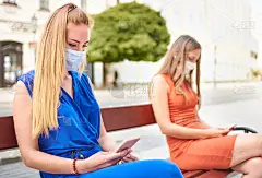 年轻女性朋友戴着口罩用手机使用社交网络-千禧女孩保持距离防止病毒传播-新的正常生活理念