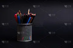 将钢笔和铅笔放置在桌面的黑色背景上，留出复印的空间。一个有文具的金属桶的特写。Holder with