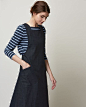 Pinafore front dress in deep, indigo-dyed denim. Slanted patch pockets. Wide straps, crossing over at back. Large, asymmetric pleat at back. Concealed side zip.