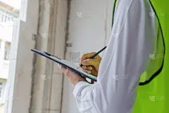 穿着绿色反光外套的验房工程师检查检查文件，并在施工现场用剪贴板检查建筑内部，施工，承包商和工程概念