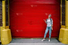 快乐的女游客喜欢花时间在户外，在红色的宣传背景下抱水提神，积极的时髦女孩使用智能手机聊天站在宣传区附