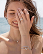 This may contain: a young woman is smiling and holding her hand up to her face with the ocean in the background