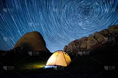 星星在山和一个发光的帐篷上空盘旋