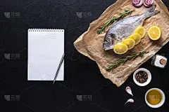 生的多拉多放在烹饪纸上，配上香料和一个笔记本，用来做菜谱或菜单。
