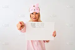 中年妇女戴着睡眠面罩穿着睡衣举着旗帜在孤立的白色背景指向相机和你，手势，积极和自信的手势从前面