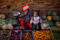 尼泊尔，巴德岗：一名女孩和妹妹在照看妈妈的蔬菜摊位时吃橘子。