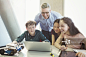 Smiling male teacher and students programming robotics at laptop in classroom