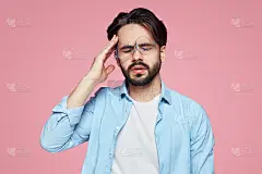 疲惫的年轻男性下班后头痛得厉害，闭上眼睛，双手放在太阳穴上，在粉红色的背景下感到疼痛