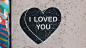 Heart-shaped street art poster against a stapled wall reads "I loved you."