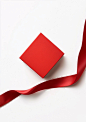 A red gift box is placed on a white background, A long ribbon gracefully floats around the square-shaped paper bag, creating an elegant and romantic atmosphere. This high-quality photo captures every detail of the paper, showcasing its texture and color. 
