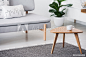 Cup on a wooden coffee table and blurry foreground with graphic pillows on a gray sofa in a white living room interior