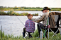 Back view portrait of loving grandfather and boy fishing by lake together during camping trip in nature, senior male stroking head of boy, copy space. outdoor portrait. fishing activity concept