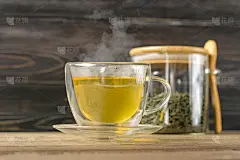 玻璃透明杯热气腾腾的绿茶，可以用茶叶和勺子放在木桌上健康饮料，抗压力饮料的概念