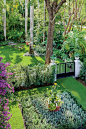 Geometric planting beds (parterres) in the front yard showcase annuals, perennials, and evergreen shrubs. A gorgeous purple-flowering bougainvillea vine is trained against the home's front wall. The formality out front contrasts strikingly with the flowin