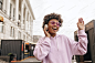 Cheerful happy brunette curly African woman in hoodie and pink sunglasses listens to music in headp