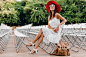 Attractive woman dressed in white dress, red hat, sunglasses sitting in summer open air theatre on chair alone, spring street style fashion trend, accessories, traveling with backpack